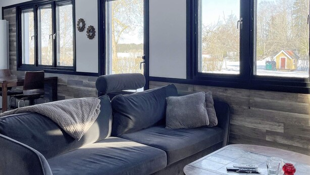 A modern living room with a grey sofa, a round coffee table, and large windows offering a view of a snowy landscape.