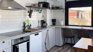 A modern kitchen with white cabinetry, a built-in oven, a coffee maker, and a window with a view of the outside.