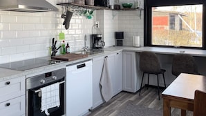 A modern kitchen with white cabinetry, a built-in oven, a dishwasher, and a window with a view of the outside.