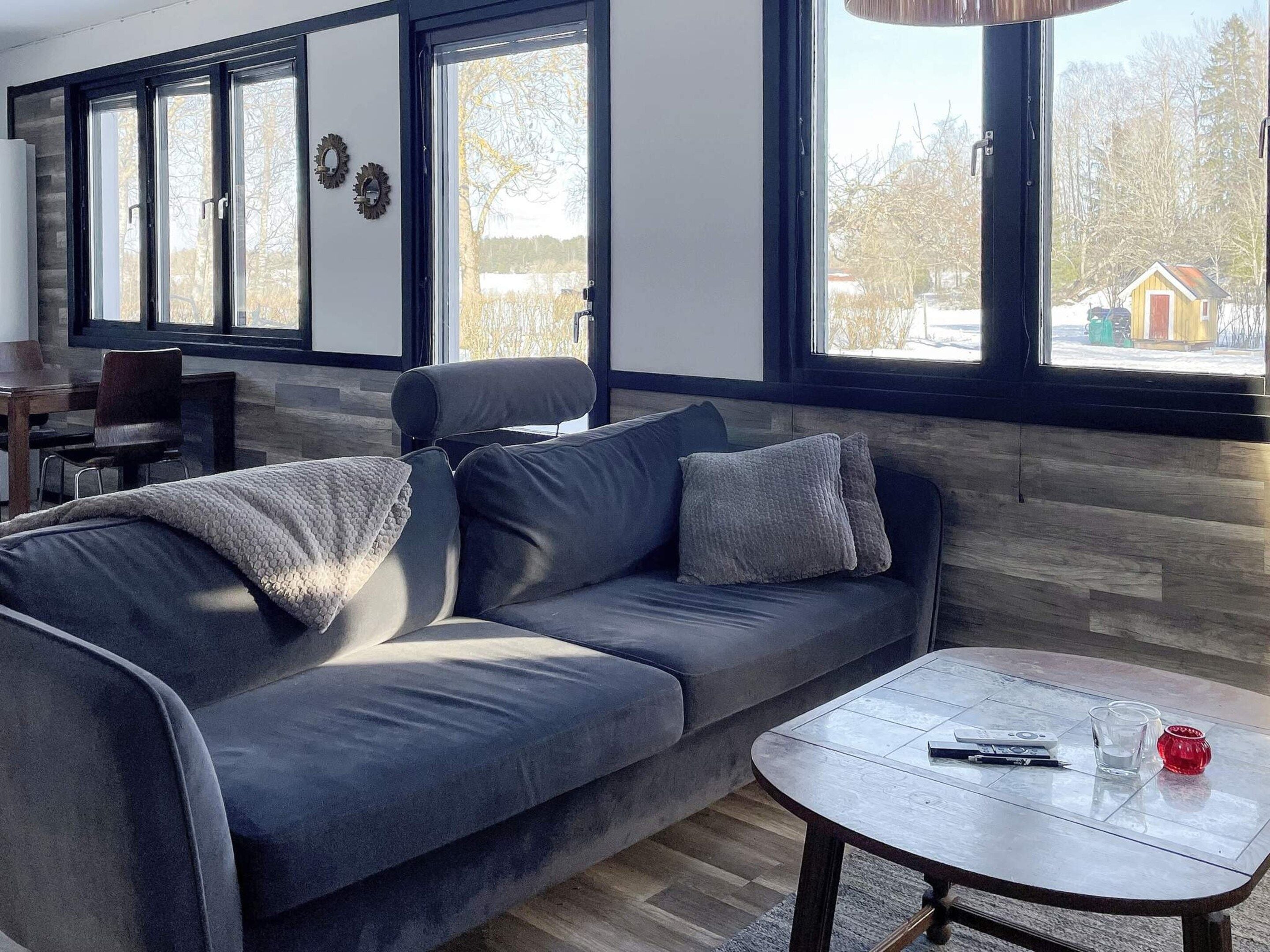 A modern living room with a grey sofa, a round coffee table, and large windows with a view of a snowy landscape.