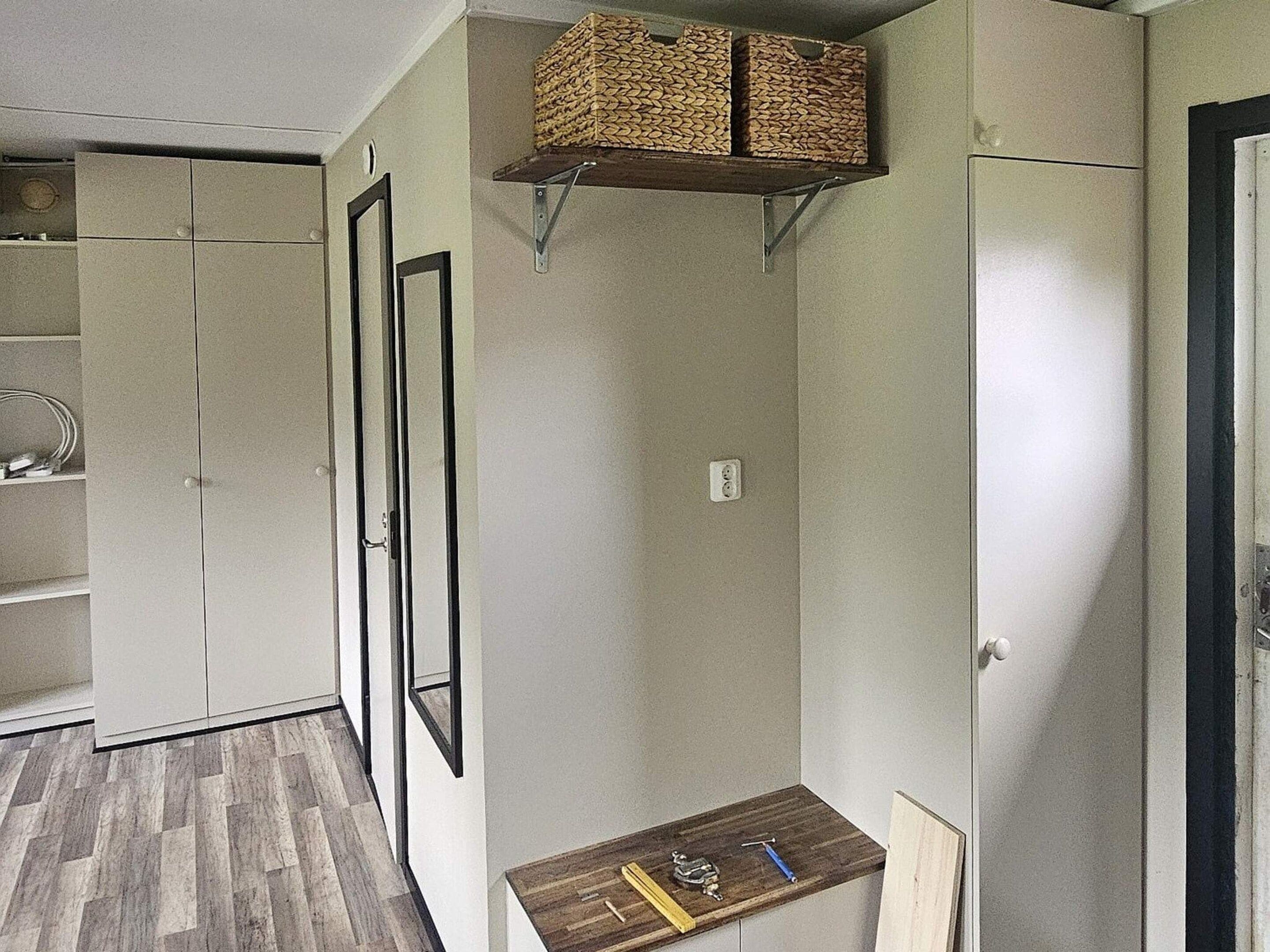 Una habitación con un armario, una estantería con cestas y una pequeña mesa con herramientas.