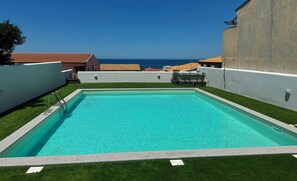 A rectangular swimming pool with a clear blue water, surrounded by white walls and green artificial grass.