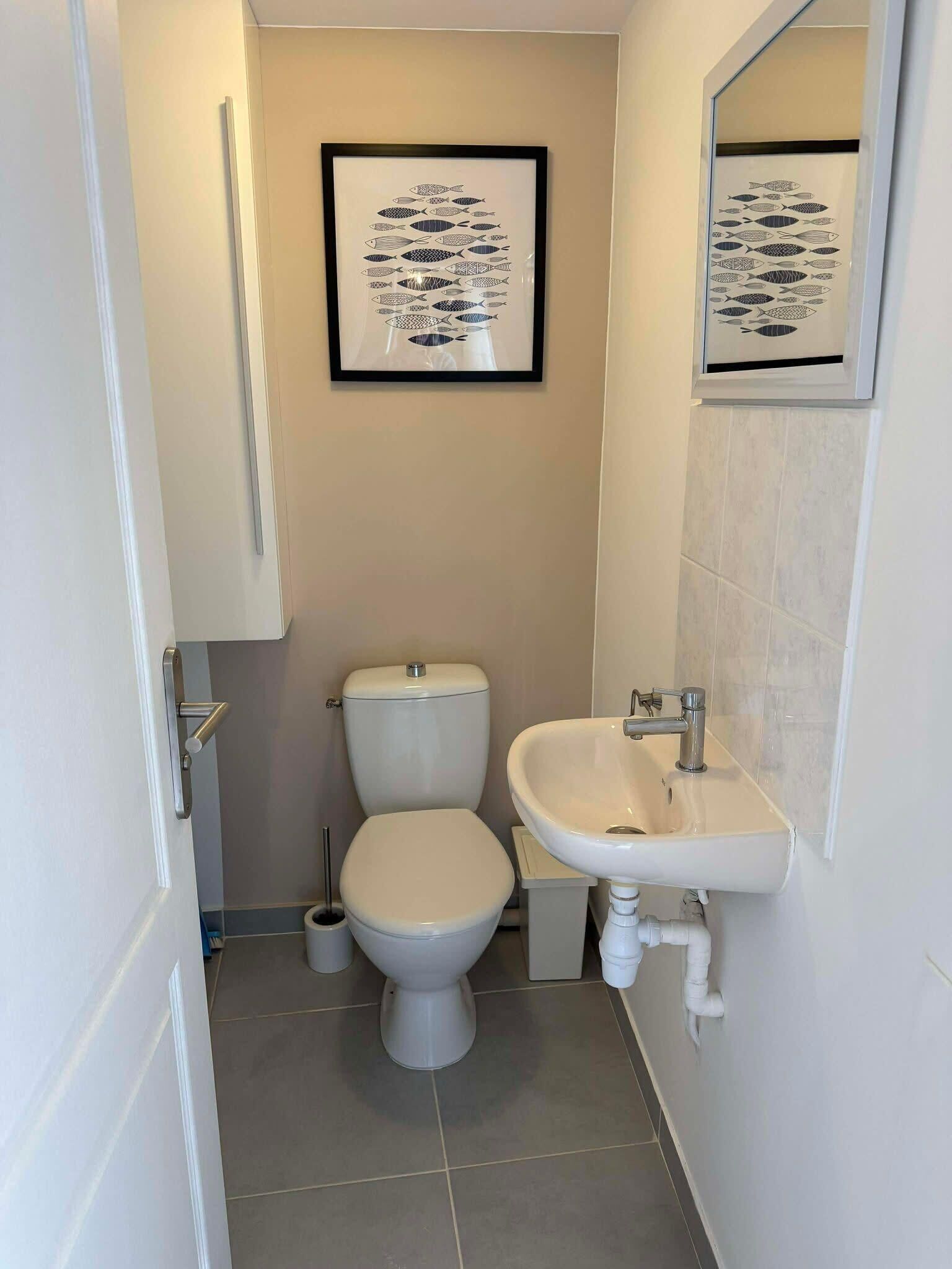 A small, clean bathroom with a toilet, sink, and framed artwork on the wall.