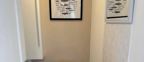 A small, clean bathroom with a toilet, sink, and framed artwork on the wall.