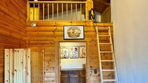 Interior de una cabaña de madera con un dormitorio en altillo, una chimenea y una escalera que lleva al área de descanso superior.