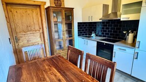 Una mesa de comedor de madera con sillas, una cocina con salpicadero de azulejos negros y un techo de madera.