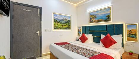 Habitación de hotel con cama, mesita de noche, escritorio y puerta. Dos cuadros decoran las paredes.
