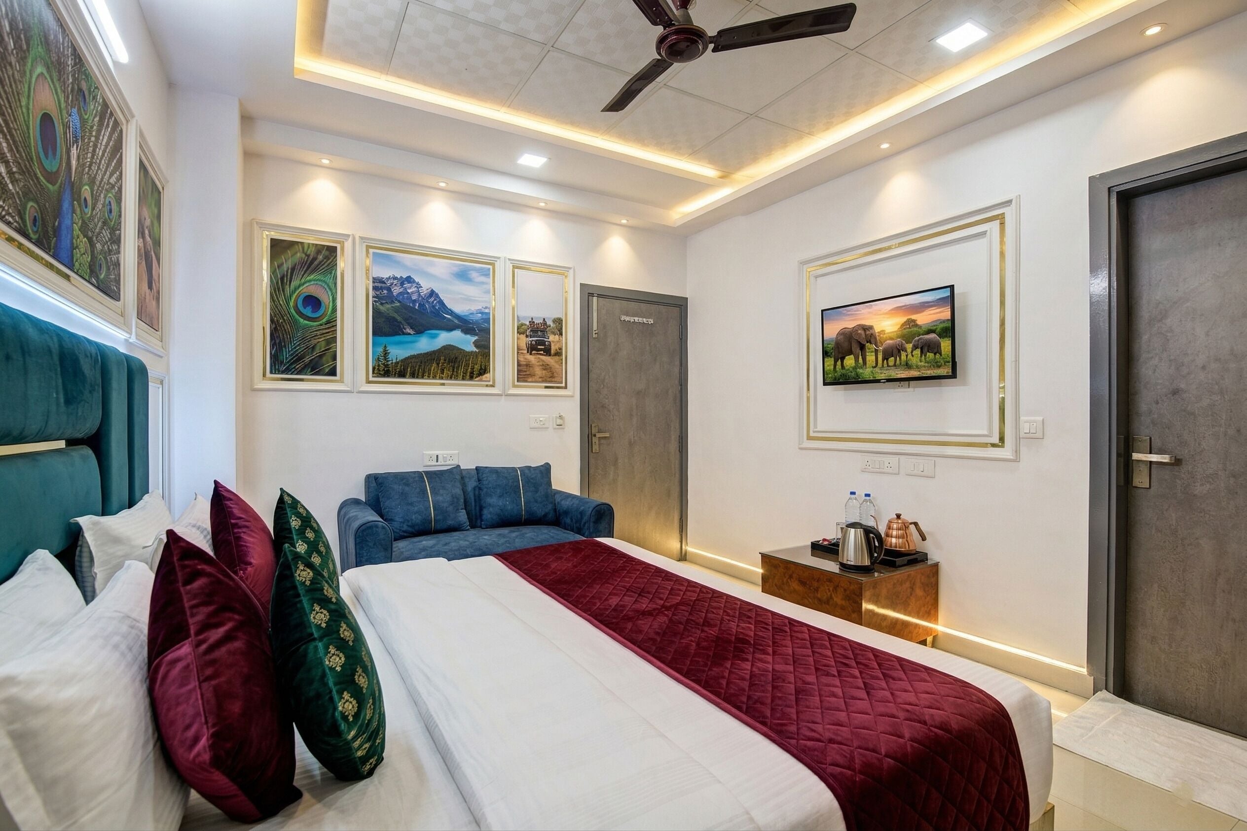 A hotel room with a bed, a blue sofa, a small table with a kettle, and framed pictures on the walls.