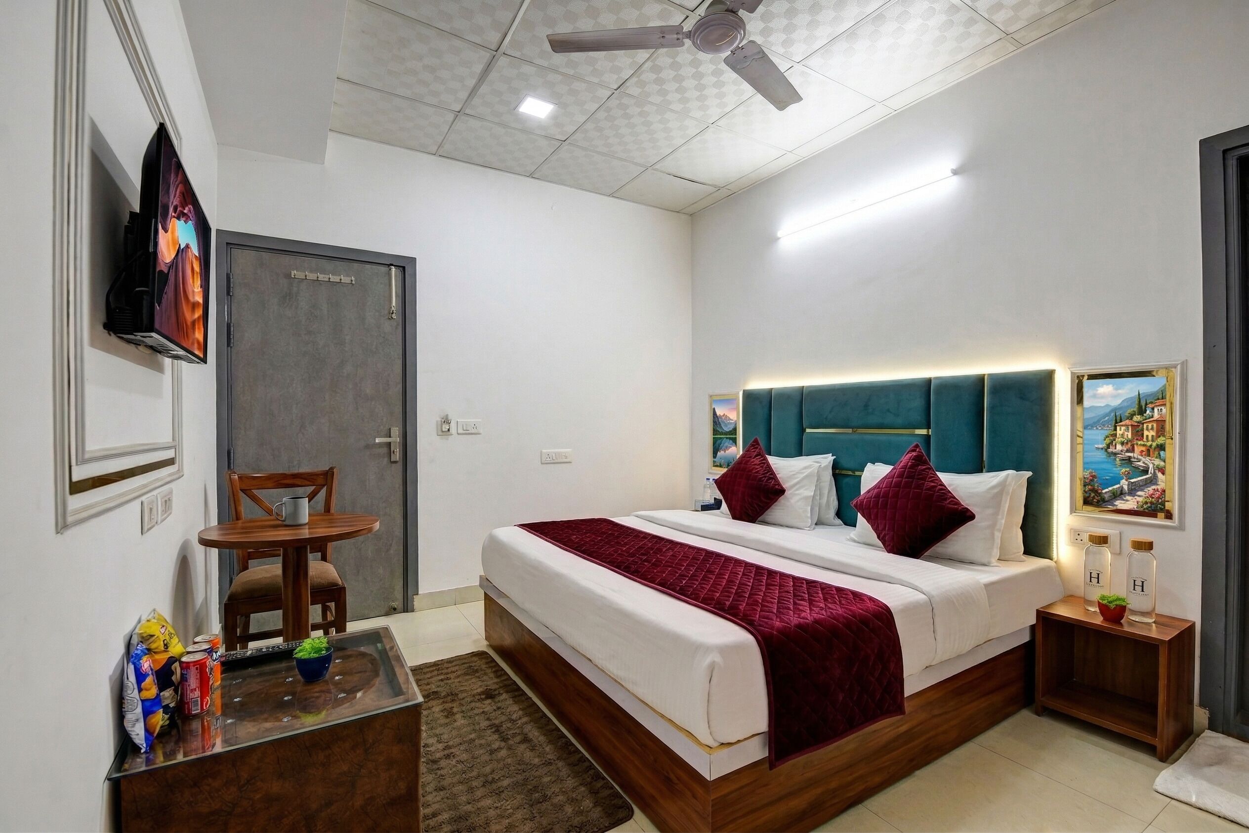 A hotel room with a bed, a desk, a chair, a television, and a painting on the wall.