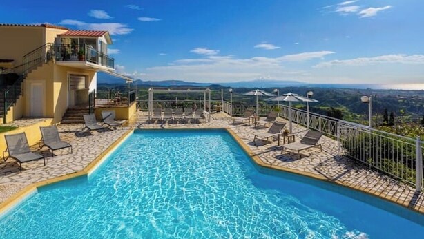 Una piscina con lettini e un balcone con vista su un paesaggio montuoso.