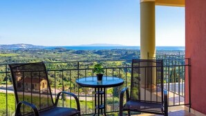Un balcone con tavolo e sedie, che si affaccia su un paesaggio verde e colline lontane.