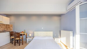 Una camera da letto con un letto, un comodino, una sedia, un tavolino con una lampada e un angolo cottura con lavandino e pensili.