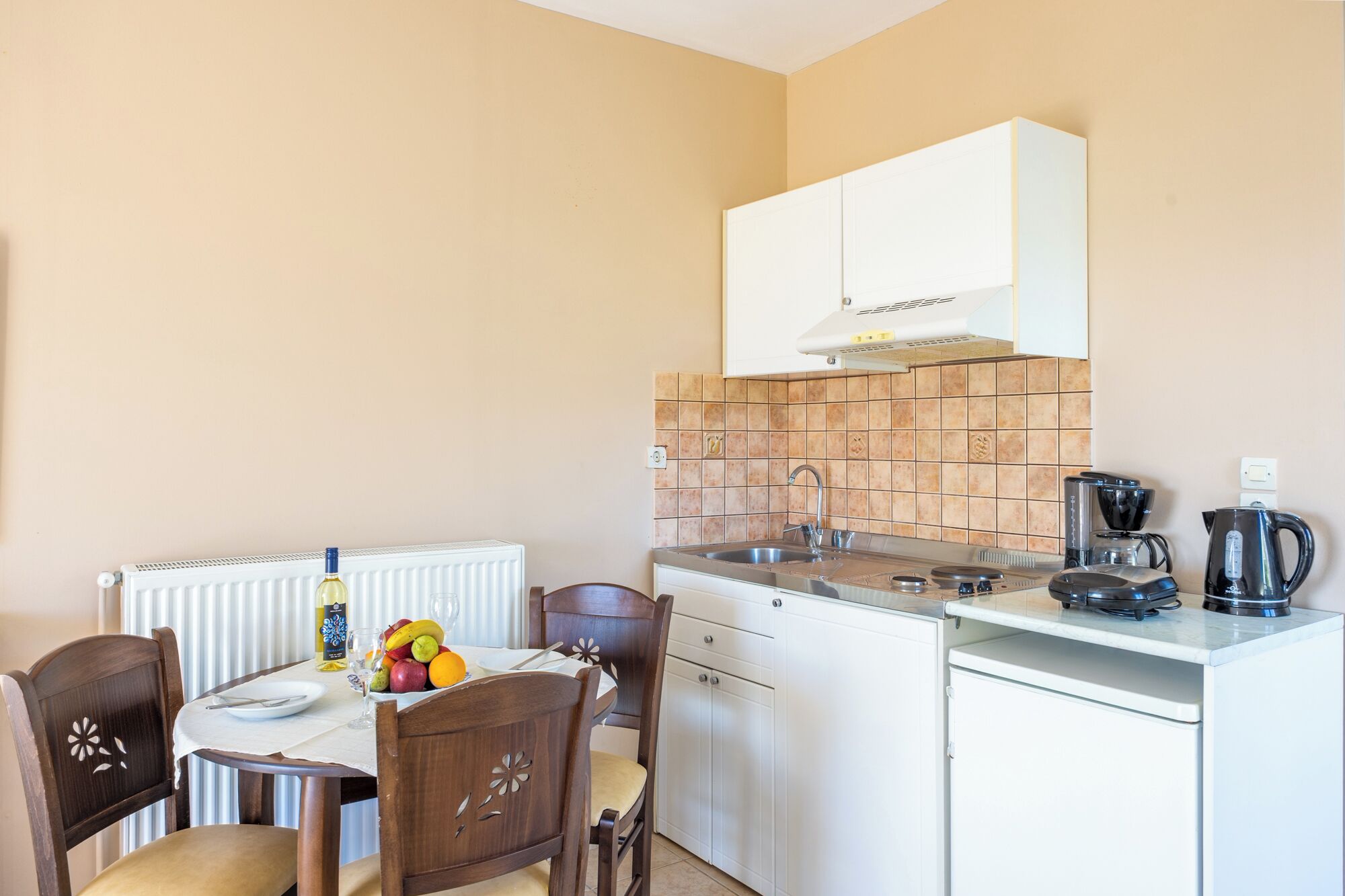 A compact kitchen with white cabinets, a built-in oven, a coffee maker, and a fruit bowl on the counter.
