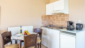 Una cucina compatta con mobili bianchi, forno integrato, macchina da caffè e una ciotola di frutta sul piano di lavoro.