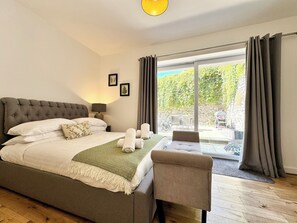 A bedroom with a large bed, a chair, a table, and a view of the outdoors. - The Barn in Courtyard, 3 -Bed, Sleeps 5, Long Term Rental Available (Ulverston)