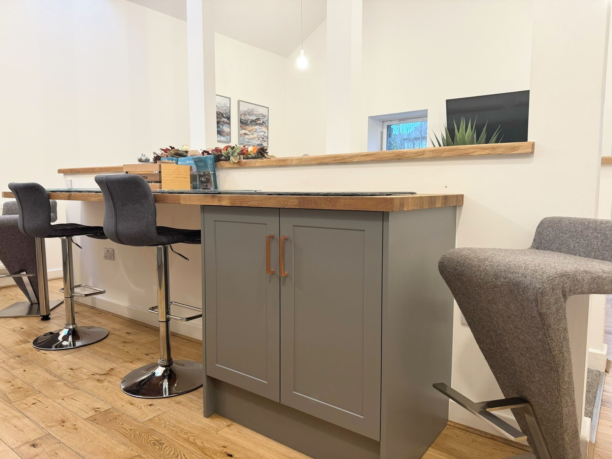 Une cuisine moderne avec des meubles gris, un plan de travail en bois et deux tabourets de bar.
