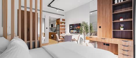 A modern bedroom with a large bed, wooden shelving, a desk, and a dining area.