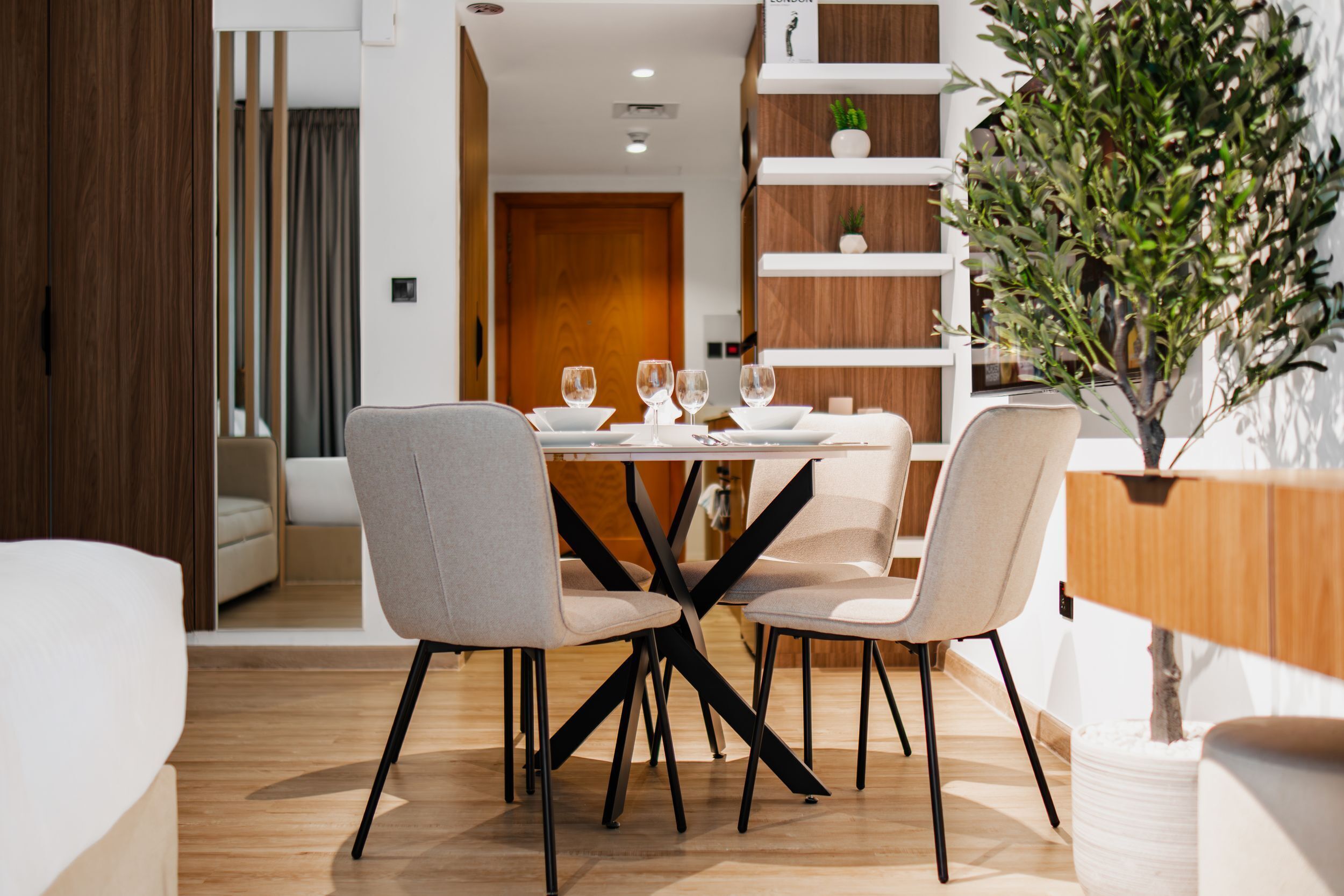 A modern dining area with a round table, four chairs, and a potted plant.