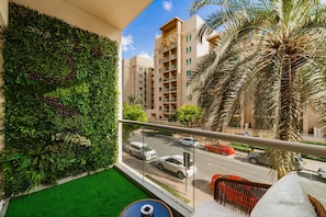 Un balcón con un muro verde, vista a una calle y una palmera.