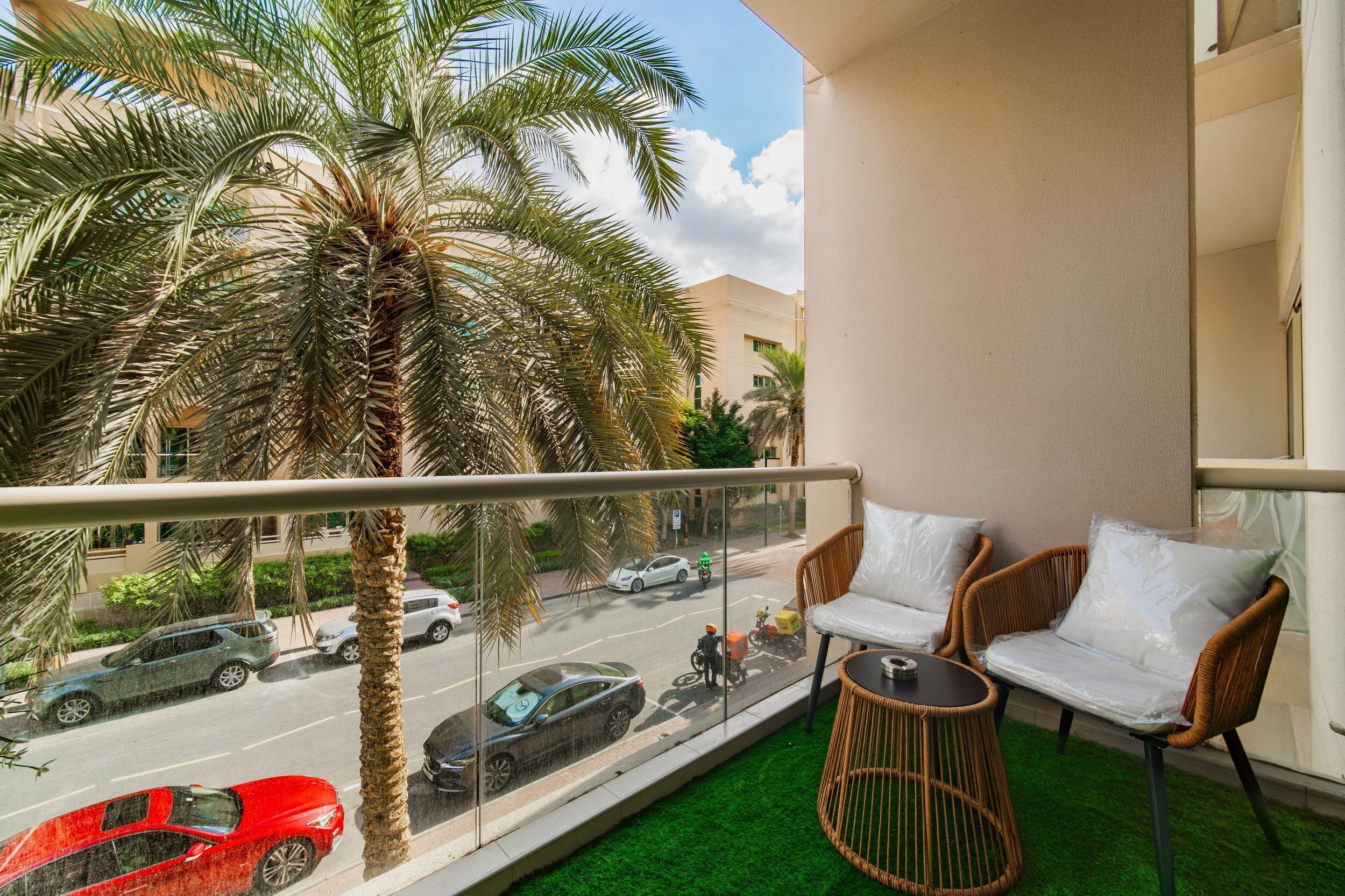 A balcony with a view of a street, a palm tree, and wicker furniture.