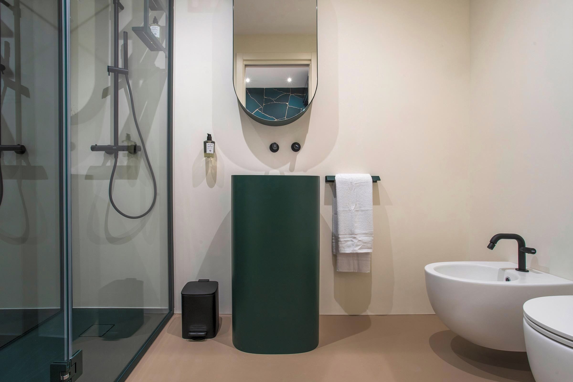 Un baño moderno con cabina de ducha de vidrio, un lavabo pedestal verde y un lavabo blanco, además de un inodoro.