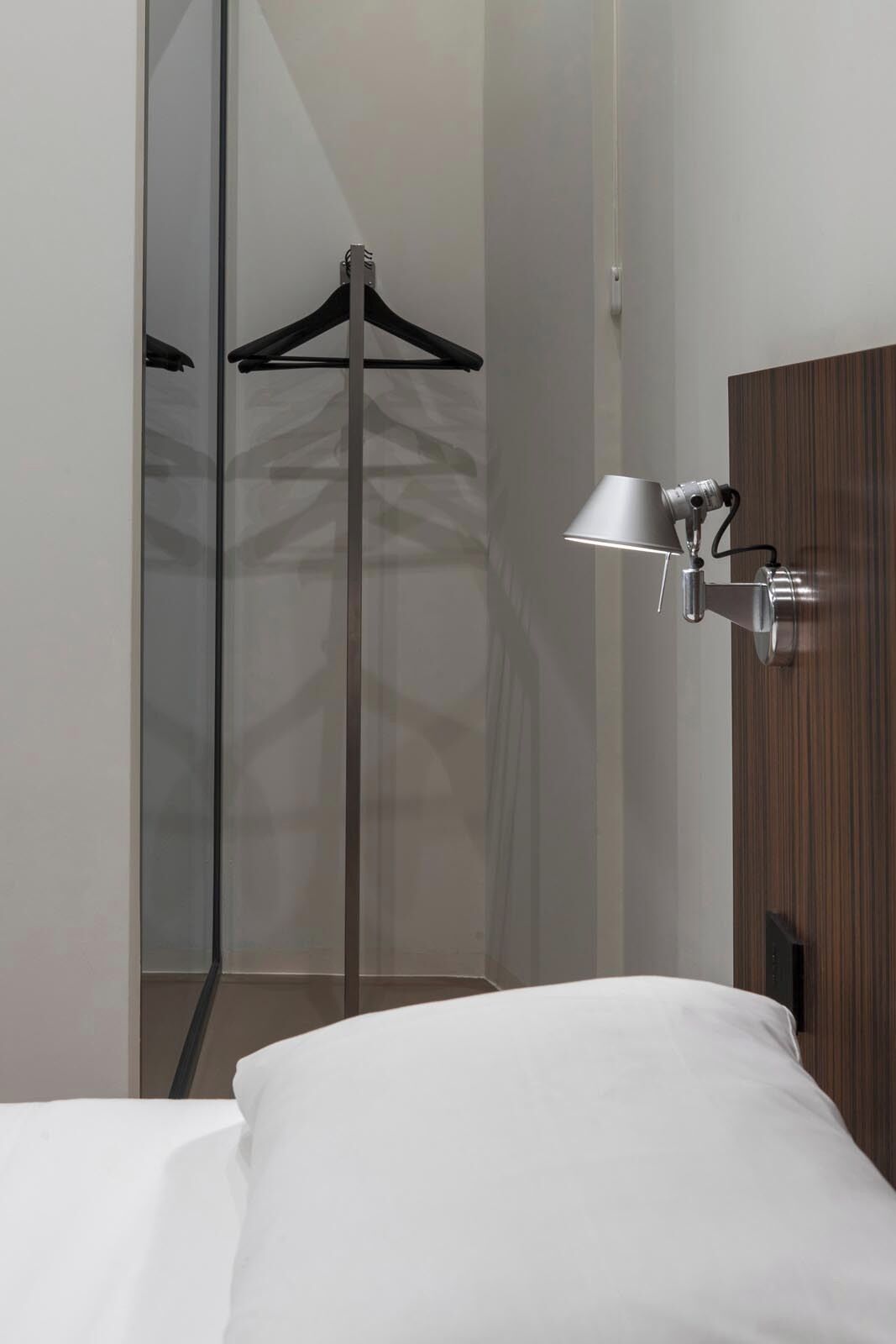 Una habitación de hotel moderna con una cama, un perchero y una lámpara de pared.