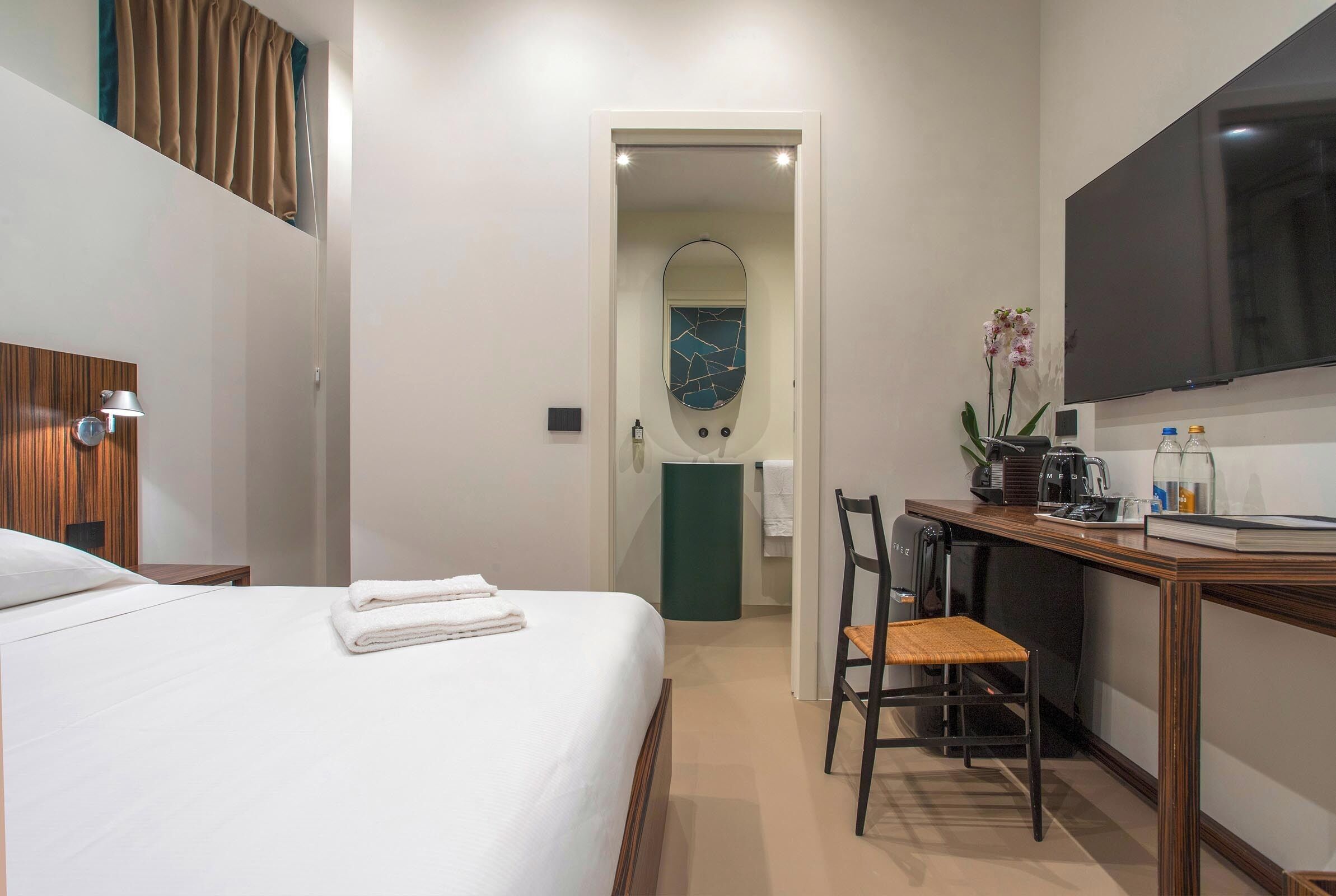 Een hotelkamer met een bed, een bureau, een stoel, een televisie en een badkamer met een spiegel.