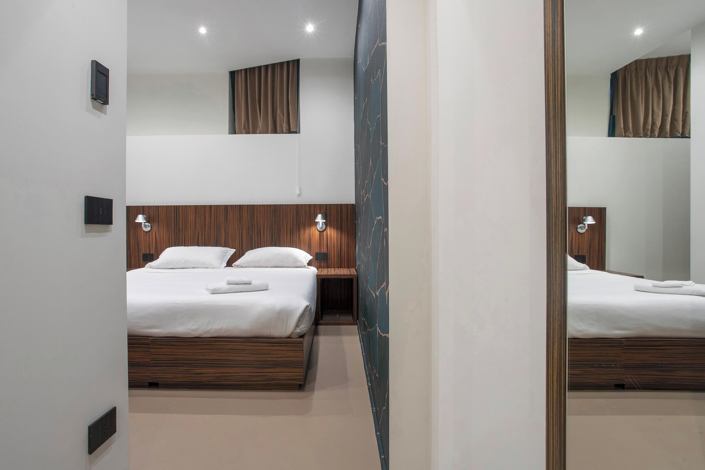 Une chambre d’hôtel avec deux lits, des têtes de lit en bois et des lampes fixées au mur.