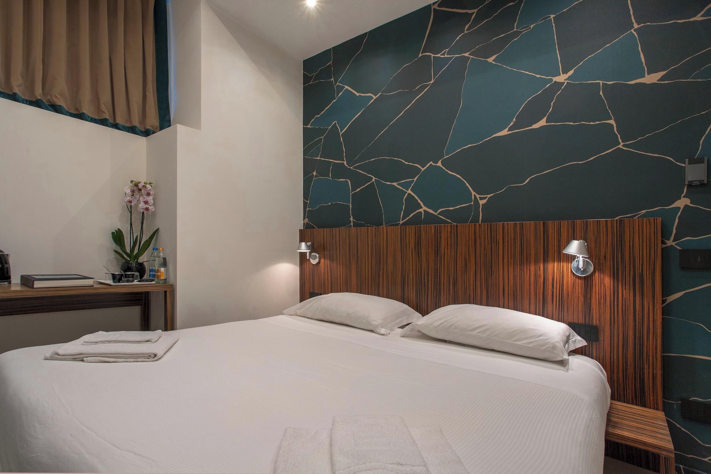 Quarto de hotel com uma cama grande, cabeceira de madeira e parede com padrão que lembra mármore.