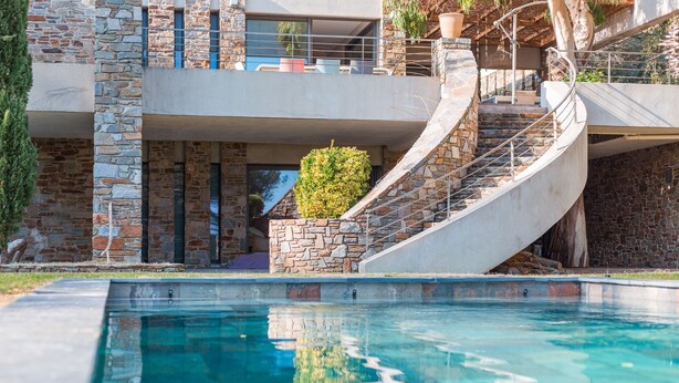Uma casa moderna com fachada de pedra, piscina e escadaria em espiral que dá para uma varanda.