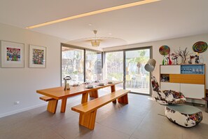 A modern dining area with a wooden table and benches, large windows, and a ceiling light fixture.