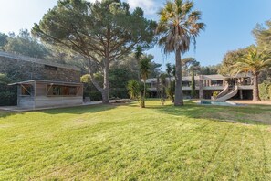A modern house with a spacious lawn, a small pool, and a stone building in the background.