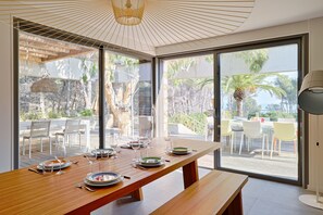 A dining area with a wooden table set for four, large windows, and a view of outdoor seating.