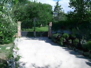 A gated entrance with a metal gate, a gravel path, and surrounding greenery.