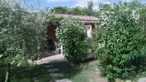 Un bâtiment rustique, doté d’un toit en tuiles, entouré d’une végétation luxuriante et accessible par un étroit sentier.