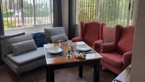 Ein Essbereich mit Tisch für zwei Personen, einem grauen Sofa und einem roten Sessel.