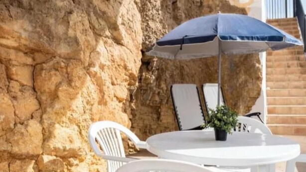 Ein weißer Sitzbereich im Freien mit Tisch und Stühlen, einem blauen Sonnenschirm und einem Blumentopf.
