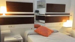 Ein kleines, ordentlich eingerichtetes Schlafzimmer mit einem Einzelbett, einem Nachttisch, einer Wandablage und einem Beistelltisch.