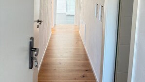 Un pasillo con suelo de madera, paredes blancas y una puerta que da a un baño.