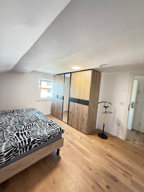 Un dormitorio con cama, armario de madera, perchero y ventana.