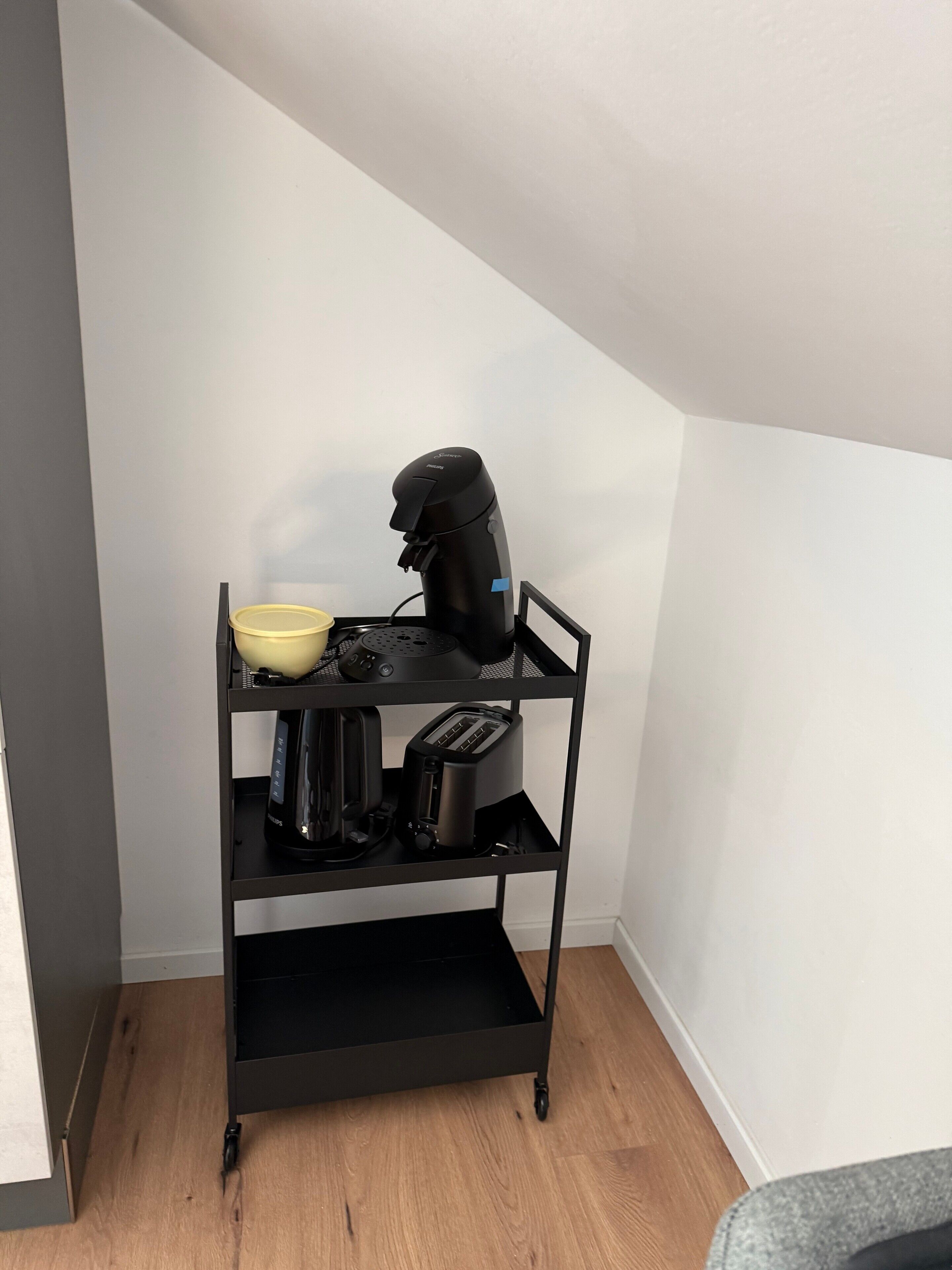 Une étagère en métal noir sur laquelle se trouvent une machine à café, un grille-pain et un bol jaune.