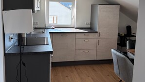 Una cocina moderna con un amplio ventanal, suelo de madera y una zona de comedor con una silla.