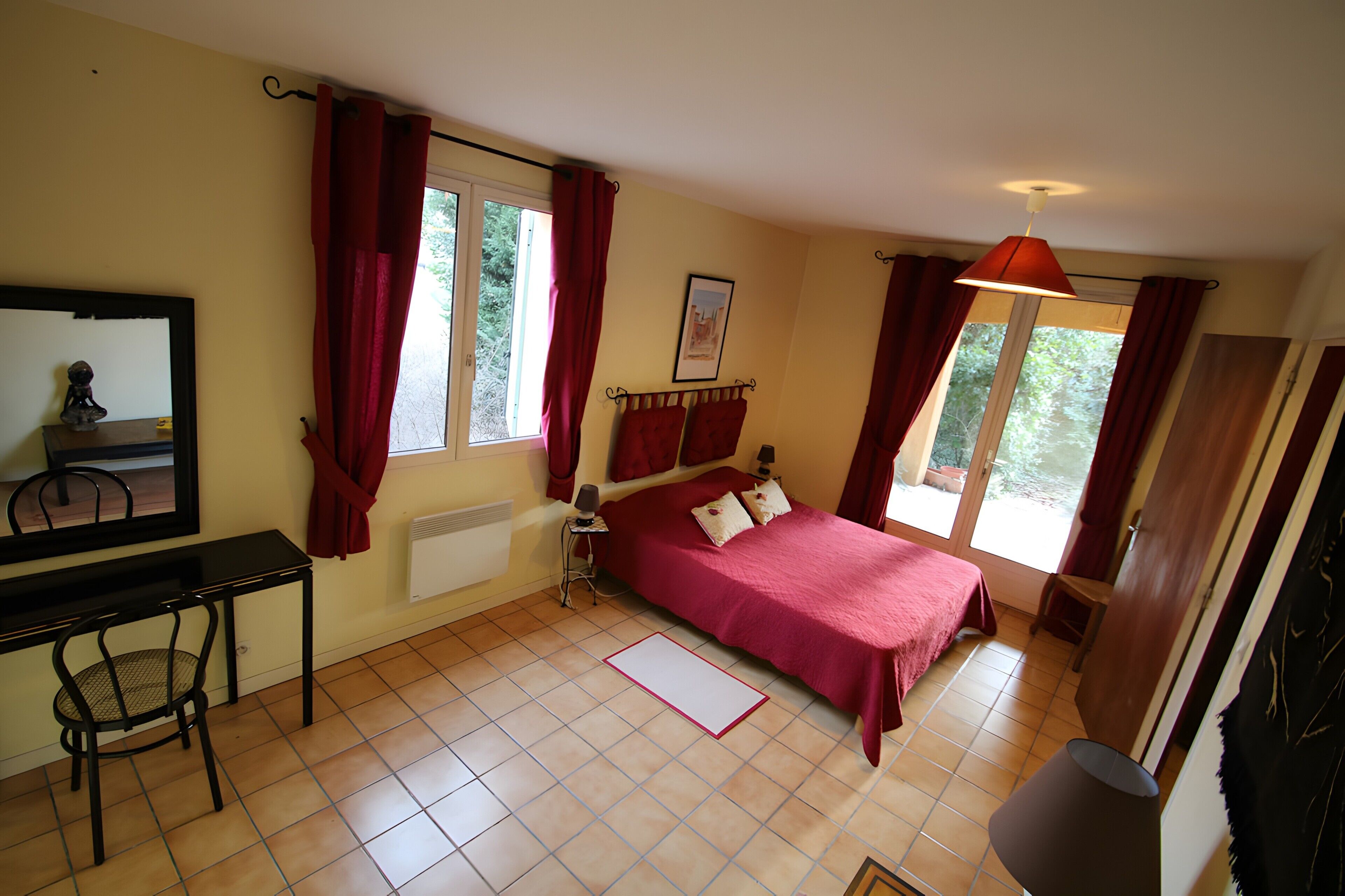 Un dormitorio con cama, escritorio, silla, ventana con cortinas y lámpara.