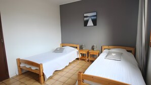 A room with two wooden beds, a small table, a chair, a desk, and a picture on the wall. - Gite la Roseraie with Pool (Ruoms)