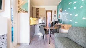 Cocina moderna con armarios de madera, comedor con mesa y sillas redondas, y pared color turquesa con calcomanías de peces.