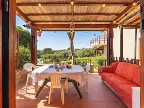 Un patio al aire libre con mesa y sillas, un sofá rojo y vistas a zonas verdes.