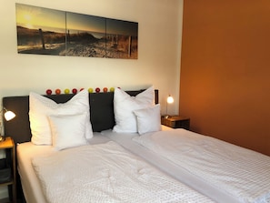 A neatly made bed with white linens, a headboard with colorful balls, and a wall-mounted picture of a beach scene. - Joanna vacation apartment with castle view in a central location (Bernkastel-Kues)