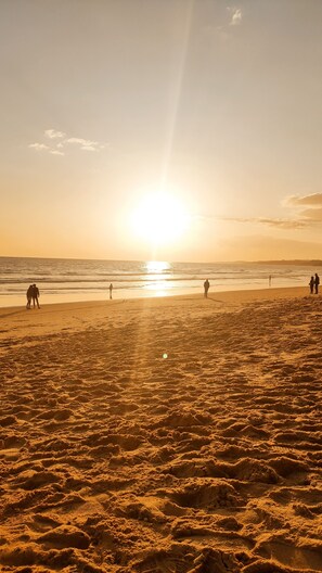 Ein Strand mit Menschen, die spazieren gehen und stehen, und die Sonne geht über dem Meer unter.