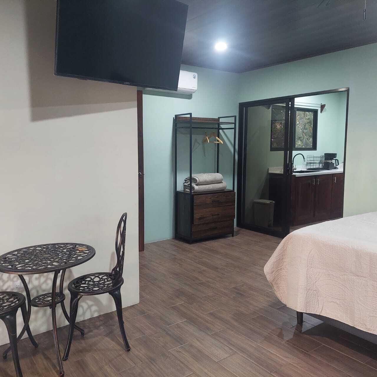 Une chambre comprenant un lit, une petite table avec des chaises, une armoire, un portant à vêtements et un téléviseur fixé au mur.