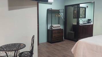 Une chambre comprenant un lit, une petite table avec des chaises, une armoire, un portant à vêtements et un téléviseur fixé au mur.